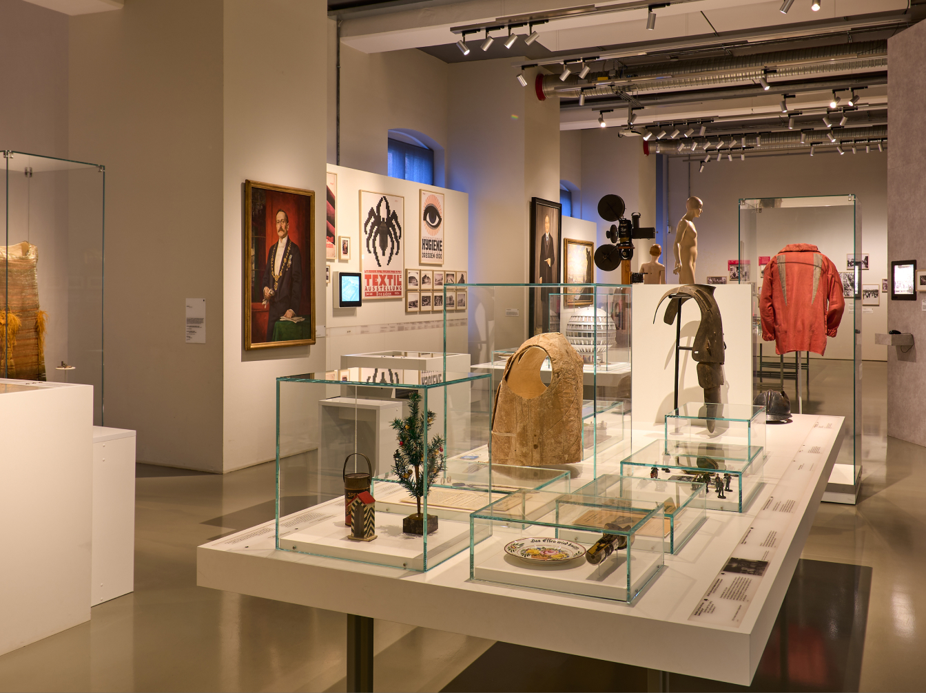 KI generiert: Das Bild zeigt eine Ausstellung in einem modernen Museum mit verschiedenen historischen und kulturellen Artefakten, die in Glasvitrinen präsentiert werden. An den Wänden sind Gemälde, Poster und andere Kunstwerke aufgehängt.