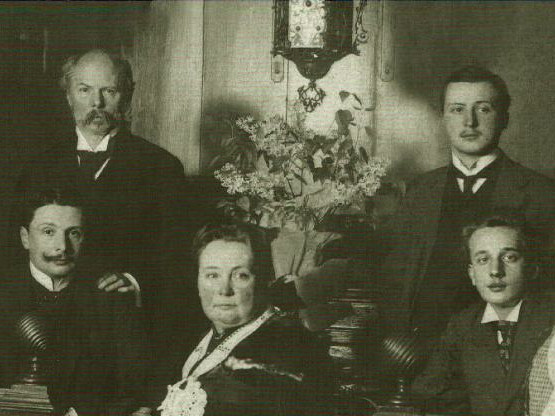 KI generiert: Das Bild zeigt eine historische Schwarzweiß-Fotografie einer Familie, die in formeller Kleidung posiert. Der Schriftzug "Die Schuchs - Eine Künstlerfamilie in Dresden" verdeutlicht, dass es sich um eine Künstlerfamilie handelt.