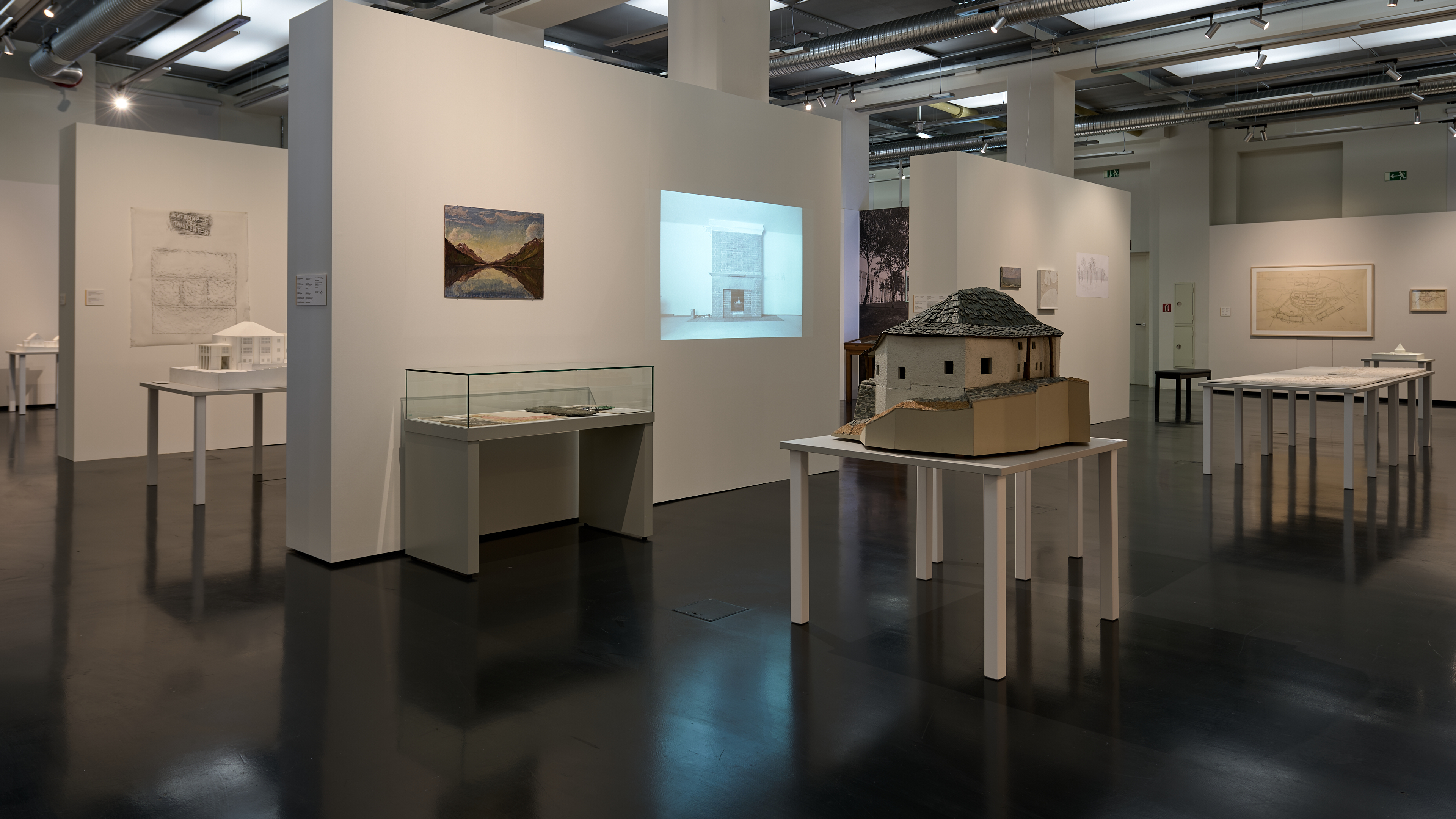 KI generiert: Das Bild zeigt eine Ausstellung mit architektonischen Modellen und Zeichnungen in einem Museumsraum. Im Vordergrund steht ein detailliertes Modell eines Gebäudes auf einem Tisch.