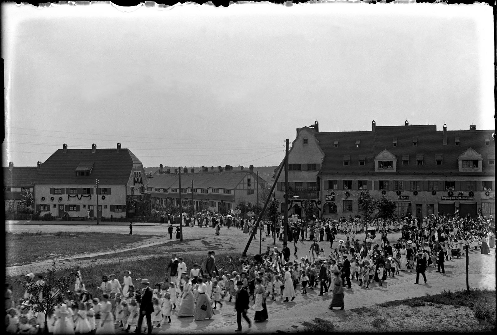 KI generiert: Das Bild zeigt einen Marsch oder Umzug mit zahlreichen Menschen, darunter viele Kinder, die durch eine städtische Straße ziehen. Im Hintergrund sind große Gebäude zu sehen, die an den Fenstern mit Dekorationen geschmückt sind, was auf ein festliches Ereignis hinweist.