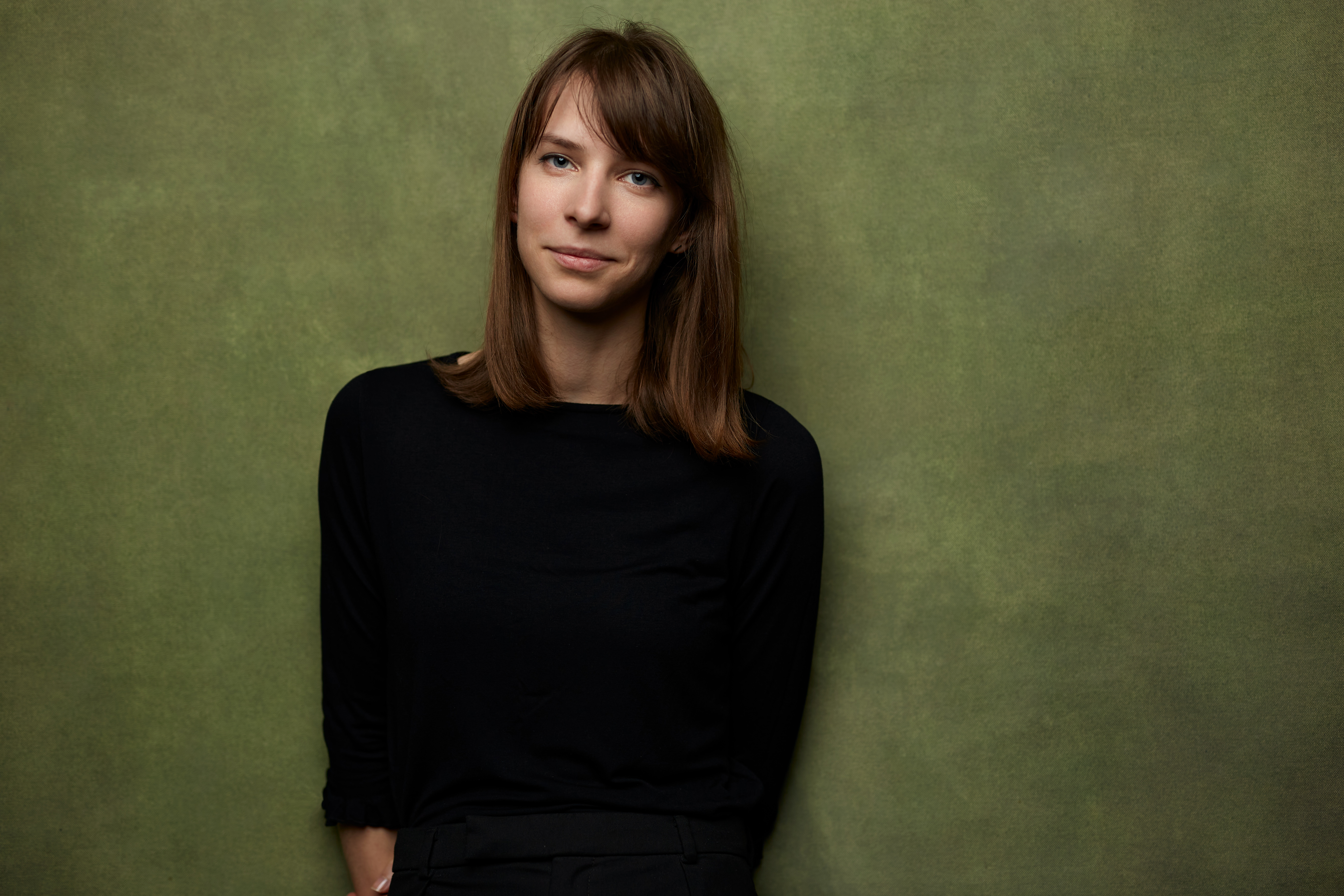 KI generiert: Das Bild zeigt eine Frau in einem schwarzen Oberteil vor einem grünen Hintergrund. Sie schaut direkt in die Kamera und wirkt entspannt.