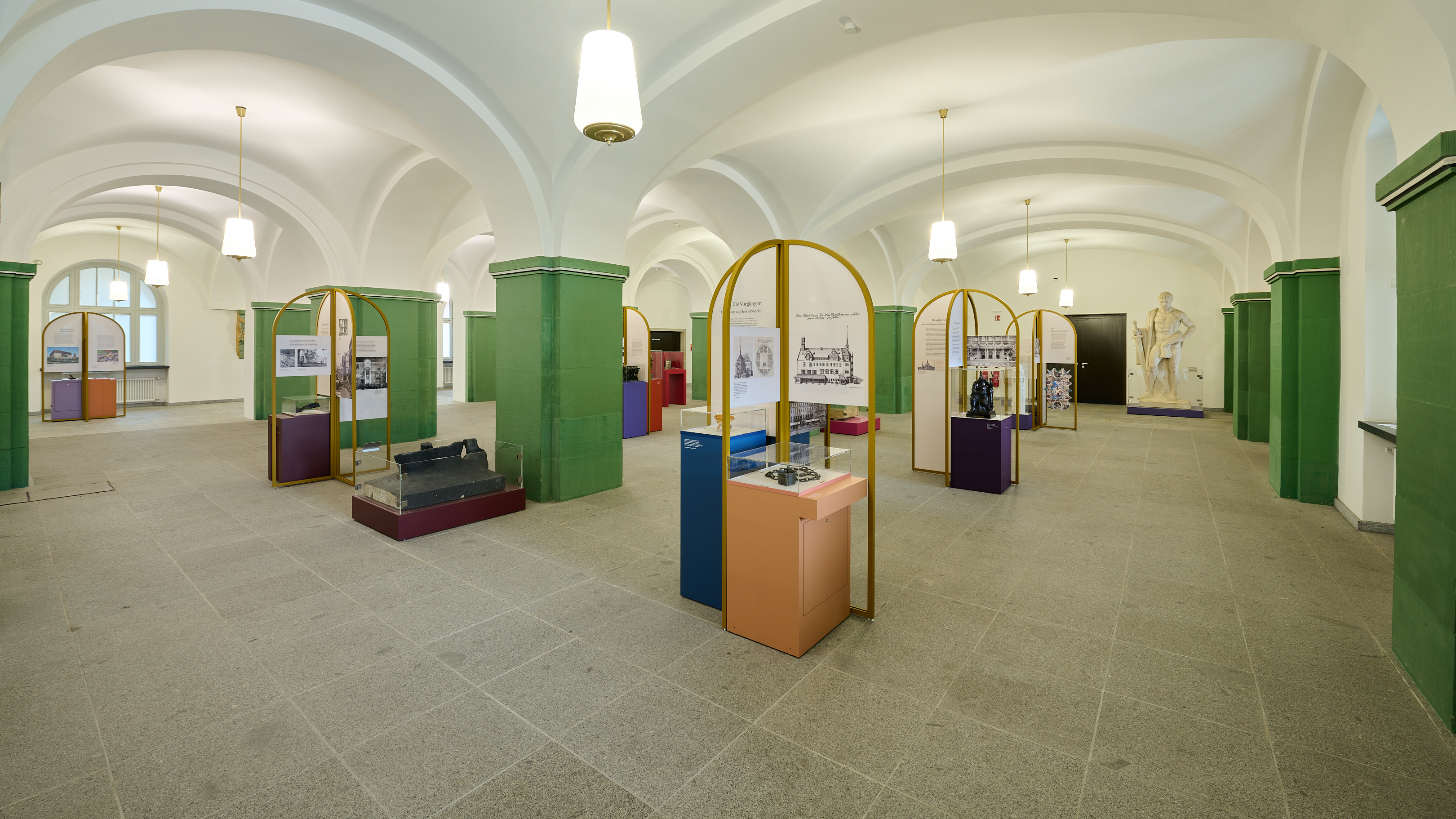 KI generiert: Das Bild zeigt eine Ausstellungshalle mit hohen Decken und mehreren beleuchteten Vitrinen, die Exponate und Informationstafeln beherbergen. Die Wände und Pfeiler sind in Grün gehalten, während der Boden scheinbar aus Steinfliesen besteht.