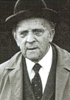 KI generiert: Das Bild zeigt einen älteren Mann in formeller Kleidung, einschließlich Hut, Hemd und Krawatte. Er hat einen ernsten oder nachdenklichen Gesichtsausdruck.