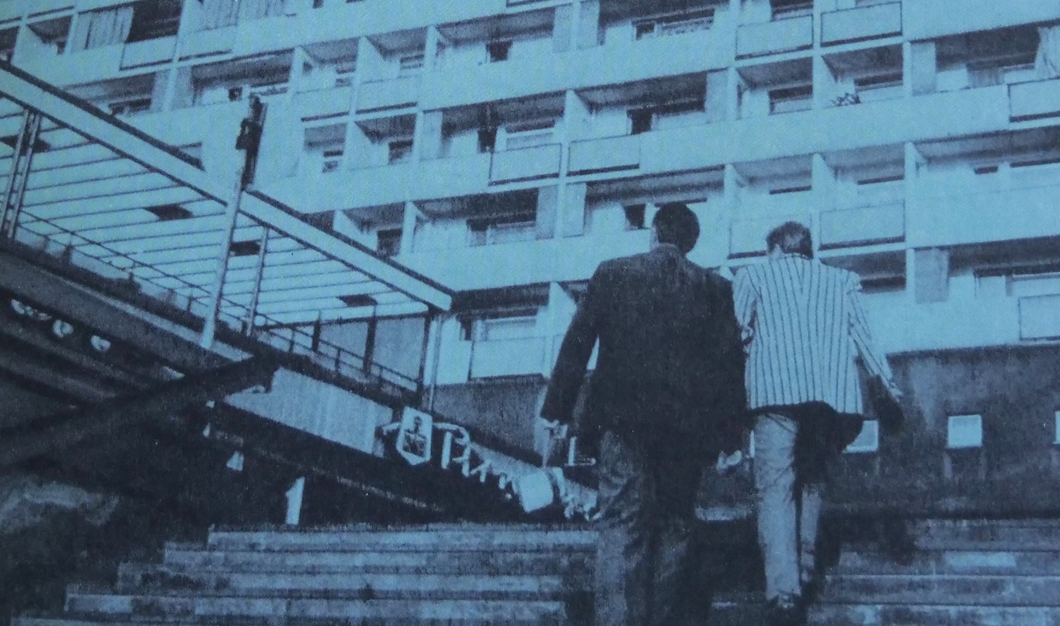 KI generiert: Das Bild zeigt ein hoch aufragendes sozialistisches Wohngebäude, vor dem zwei Personen eine Treppe hinaufgehen. Auf dem Gebäude steht ein Schriftzug und die Worte "Bau der sozialistischen Stadt" sowie "Rundgang 1" sind prominent zu sehen.