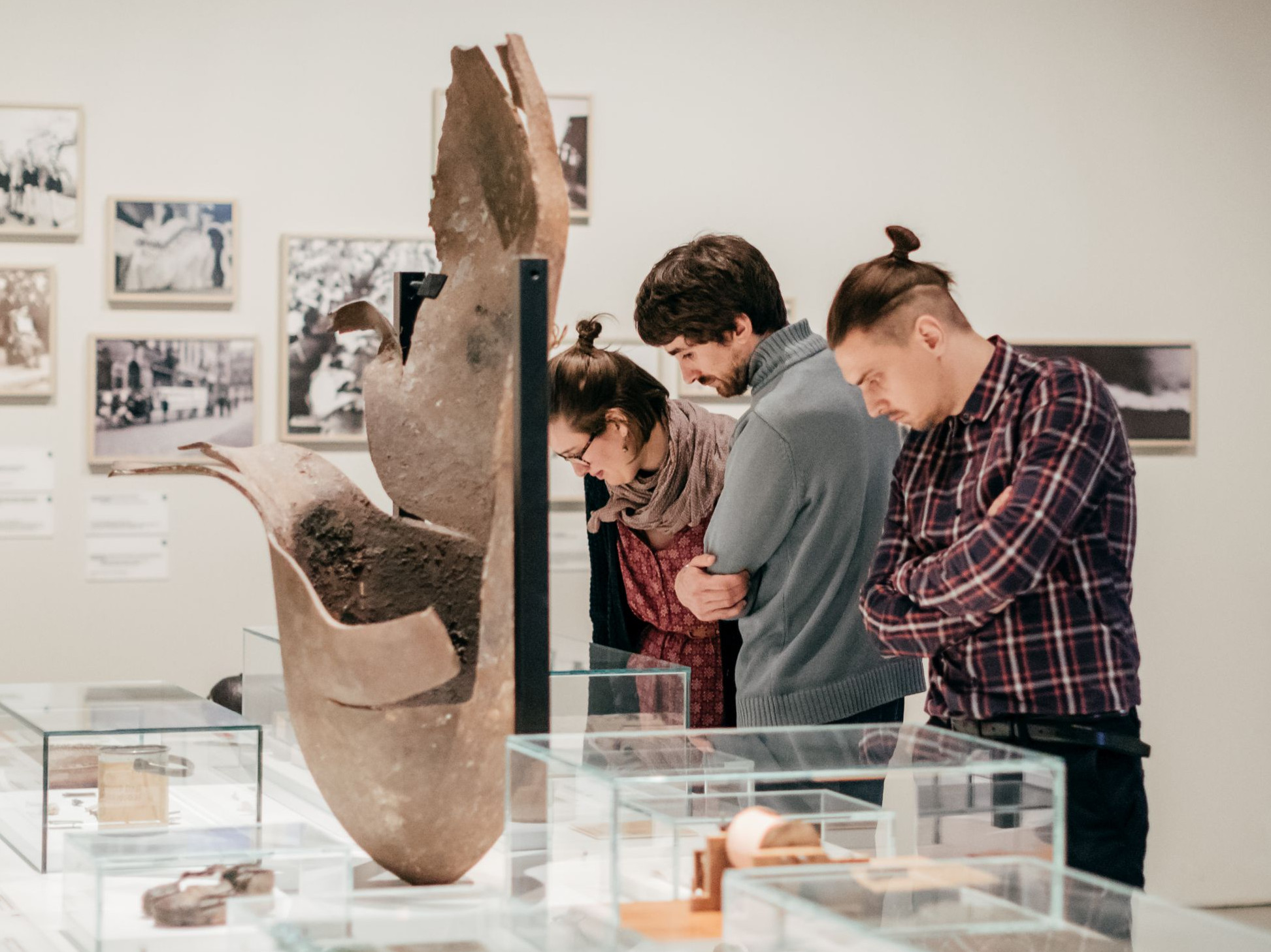 KI generiert: Das Bild zeigt eine Gruppe von Menschen, die in einem Museum Exponate betrachten. Sie betrachten Glasvitrinen und Wände mit historischen Objekten und Fotos.