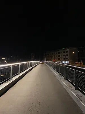 KI generiert: Das Bild zeigt eine beleuchtete Brücke in der Nacht, die sich in der Mitte des Bildes befindet. Im Hintergrund sind Gebäude mit erleuchteten Fenstern zu sehen.