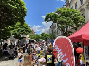 KI generiert: Das Bild zeigt eine belebte Straßenveranstaltung mit vielen Menschen, Ständen und Bäumen. Es scheint ein fröhliches Fest unter blauem Himmel zu sein.