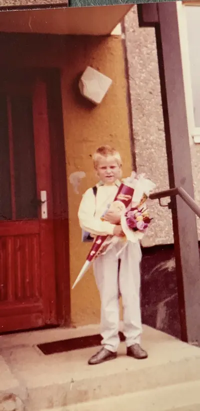 KI generiert: Ein Junge steht vor einer Haustür und hält eine Schultüte in den Armen. Er bereitet sich offenbar auf seinen ersten Schultag vor.